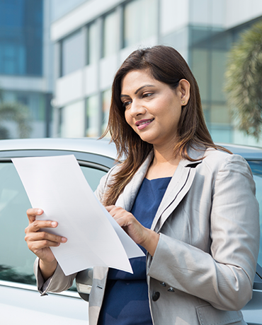 Woman reading her extended warranty paperwork by her car
