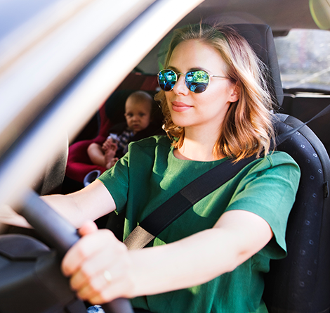 A woman with sunglasses in a car with her baby in the backseat