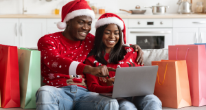 A couple dressed in Christmas sweaters and hats sitting together using their laptop.
