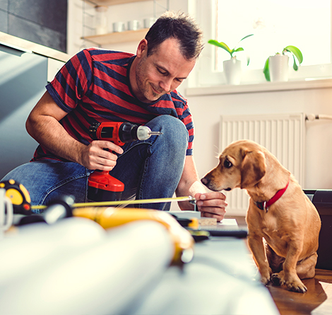 A man holding a drill and doing house work next to his dog.