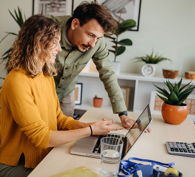 A man and woman next to each other in their home looking at a laptop.