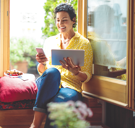 woman sitting next to window with laptop and phone