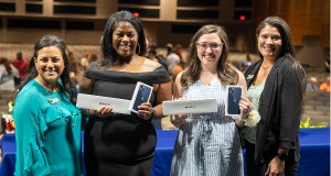 4 women standing together with two holding rewards they won.