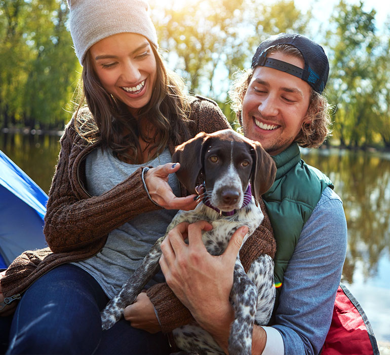 A couple sitting together outside, holding their dog.
