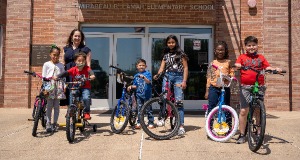 A group of kids standing outside of a school, holding their bikes.