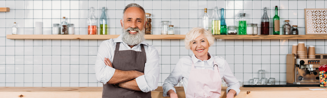 An older couple smiling at the camera in a coffee / cafe shop.