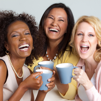 Three women holding mugs and laughing together.
