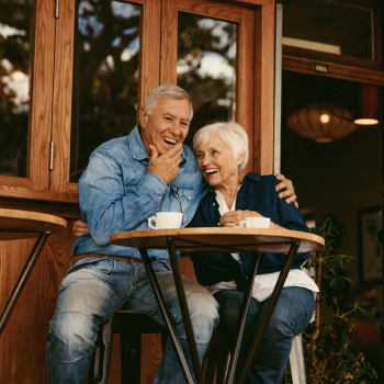 An older couple sitting together outside laughing.
